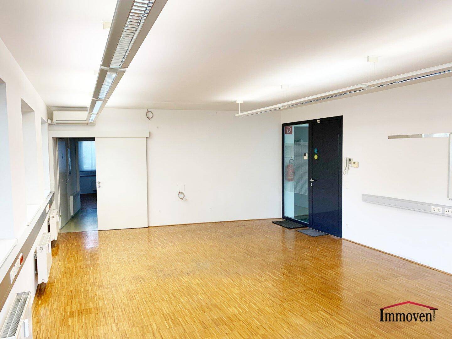 Großer Büroraum mit Parkettboden, moderner Eingangstür und viel Tageslicht, ideal für flexible Nutzung.