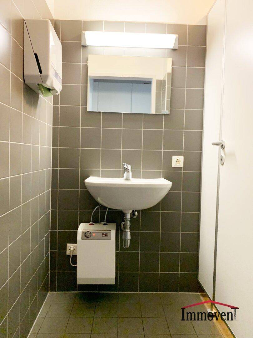 Modern gefliestes WC mit Waschbecken, Spiegel und Handtuchspender, in gutem Zustand.
