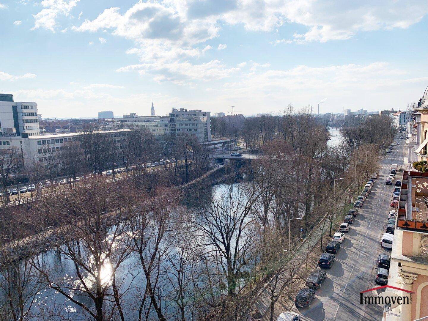 Weitläufiger Blick über einen Fluss, Bäume und die Stadtlandschaft von einem oberen Stockwerk.