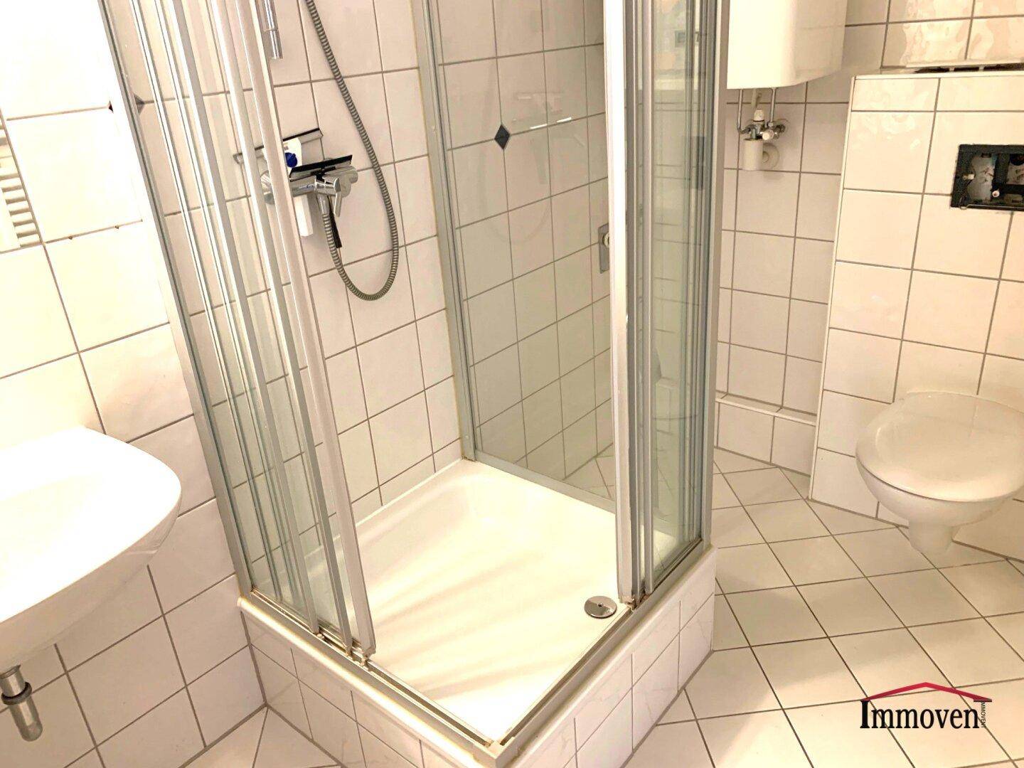 Gefliestes Badezimmer mit Duschkabine, WC und kleinem Waschbecken.