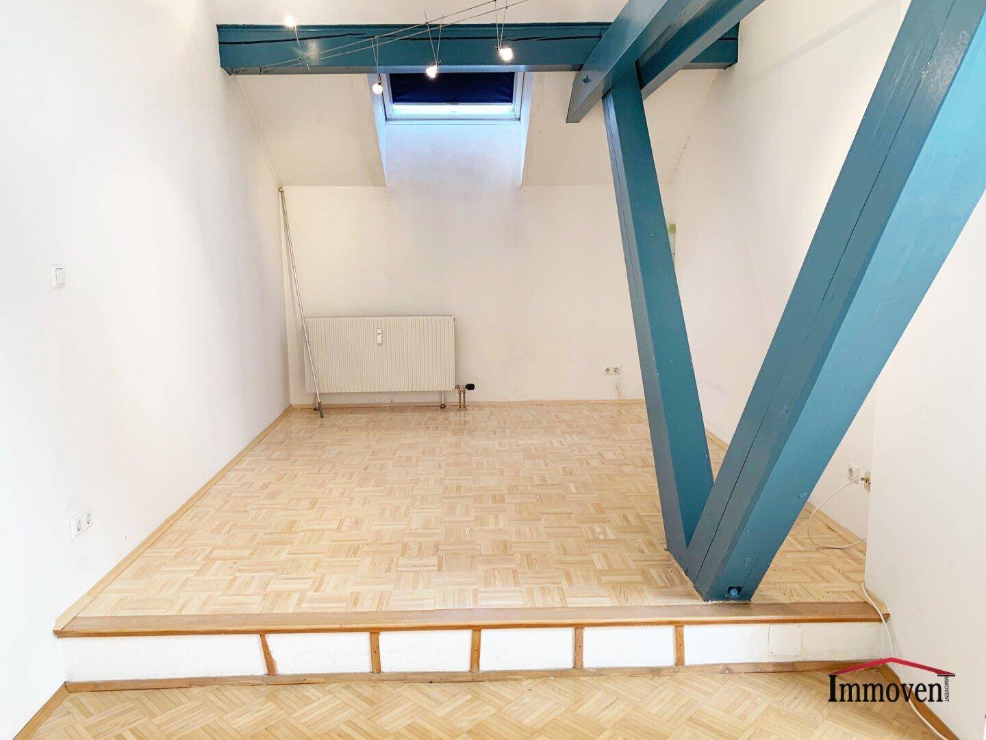 Heller Wohnbereich mit Holzbalken, Dachfenster und Parkettboden, der eine offene Atmosphäre schafft.
