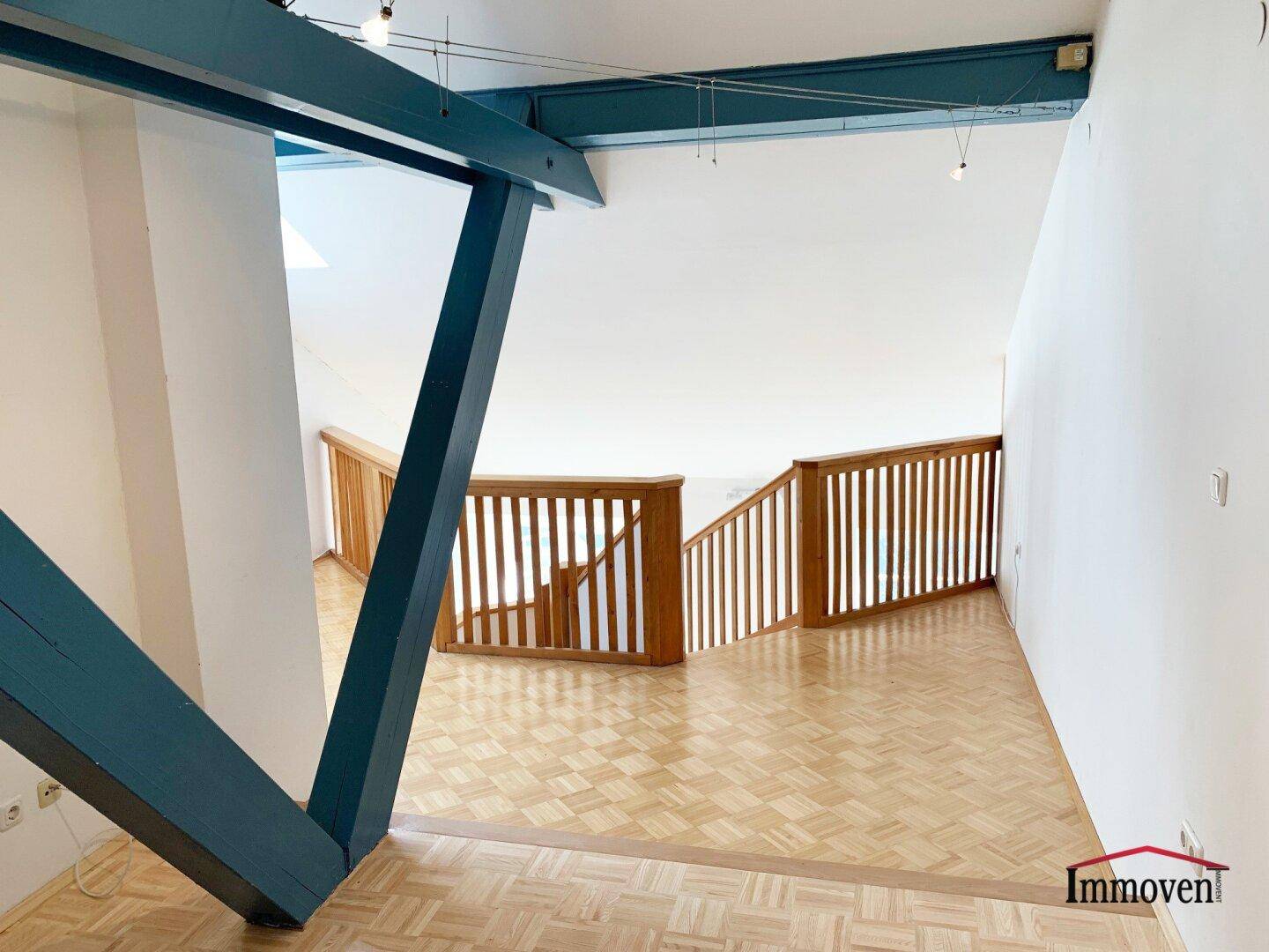 Treppenbereich mit Holzgeländer und markanten blauen Deckenbalken, die den Raum strukturieren.