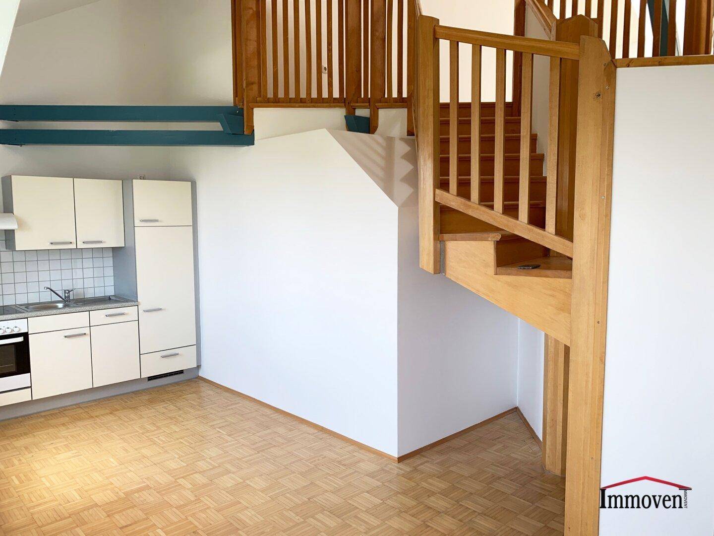 Kleine Einbauküche mit weißen Schränken und Holztreppe in einem offenen Wohnbereich.