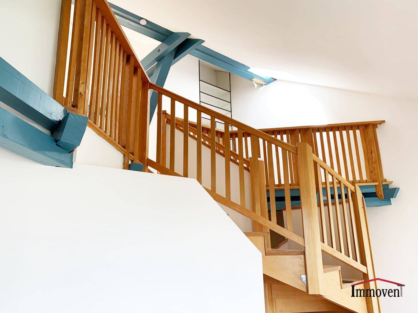 Detailansicht der Holztreppe mit Geländer und markanten blauen Deckenbalken.