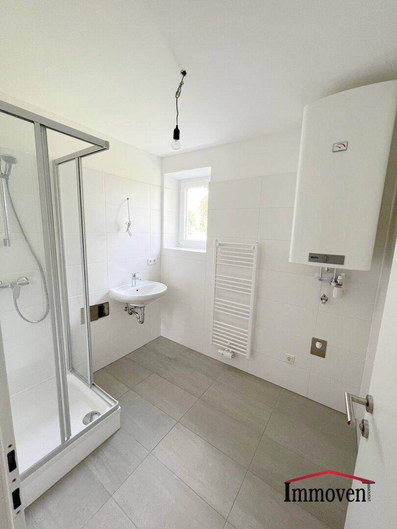 Modernes Badezimmer mit Duschkabine, Waschbecken, Fenster und praktischem Handtuchheizkörper.