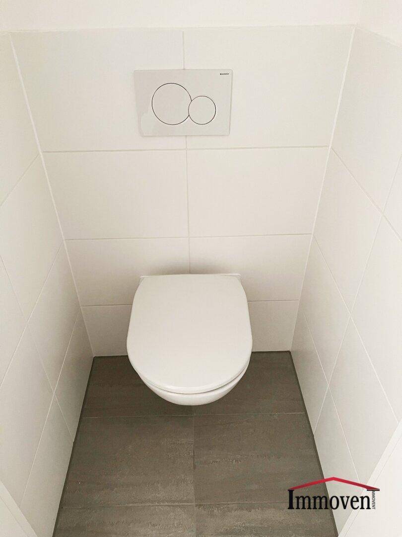 Separates WC mit Wand-WC und Fliesenboden in schlichtem, sauberem Design.