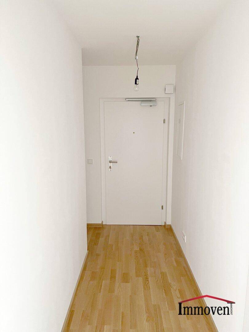 Heller Flur mit Holzfußboden und Eingangstür, der einen einladenden Empfangsbereich bietet.
