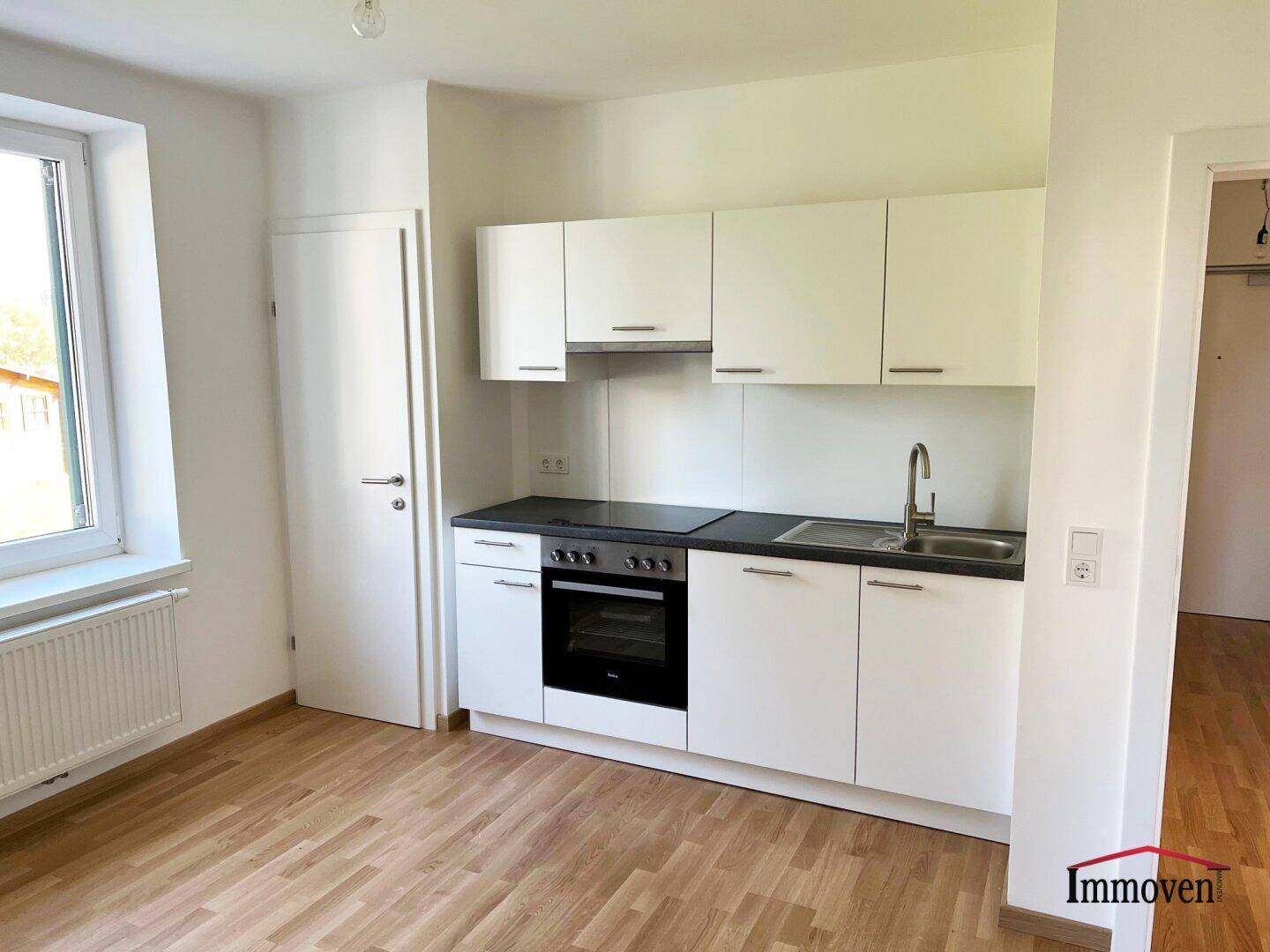 Moderne Einbauküche mit weißen Schränken, Spüle und Kochfeld in einem hellen, funktionalen Raum.