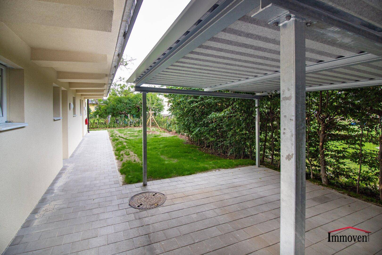 Überdachter Stellplatz oder Carport mit gepflastertem Boden und angrenzendem Grünbereich.