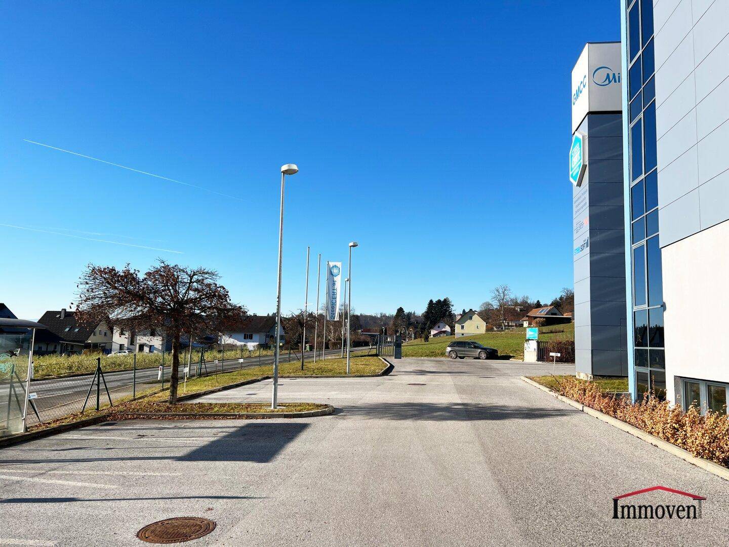 Großer Parkplatz vor dem Bürogebäude mit Laternen und umliegender Landschaft.