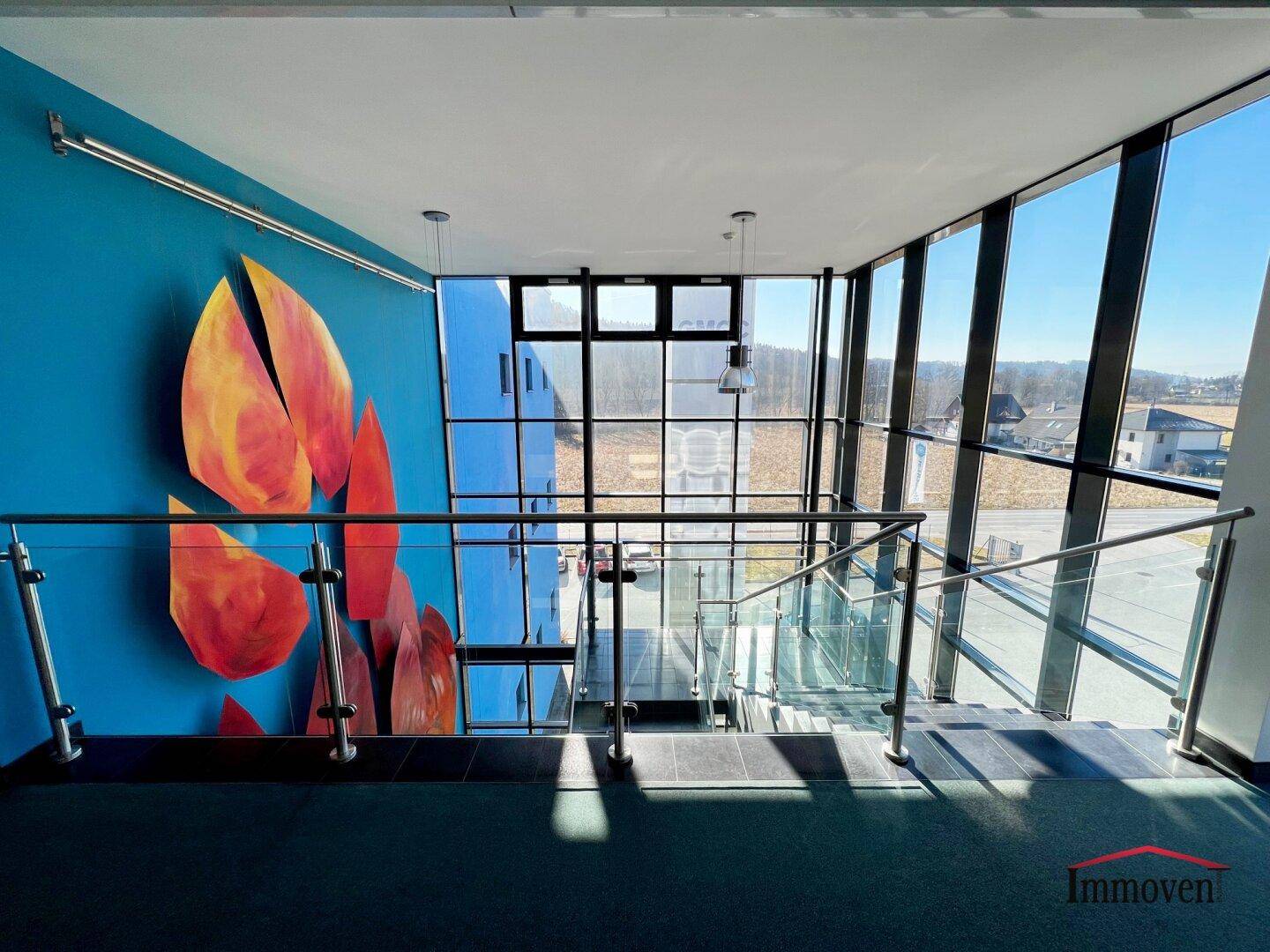 Treppenhaus mit Glasgeländer, blauer Wandgestaltung und weitem Blick nach draußen.