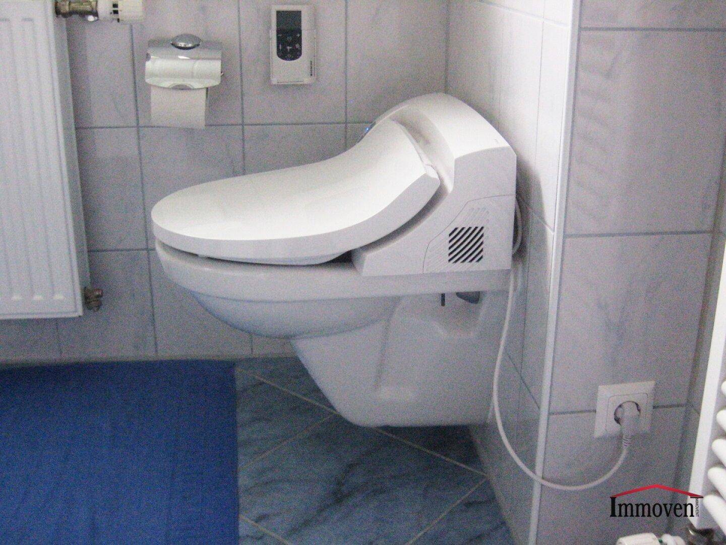Wandhängendes WC mit blauer Sitzfläche und Heizkörper in einem gefliesten Raum.