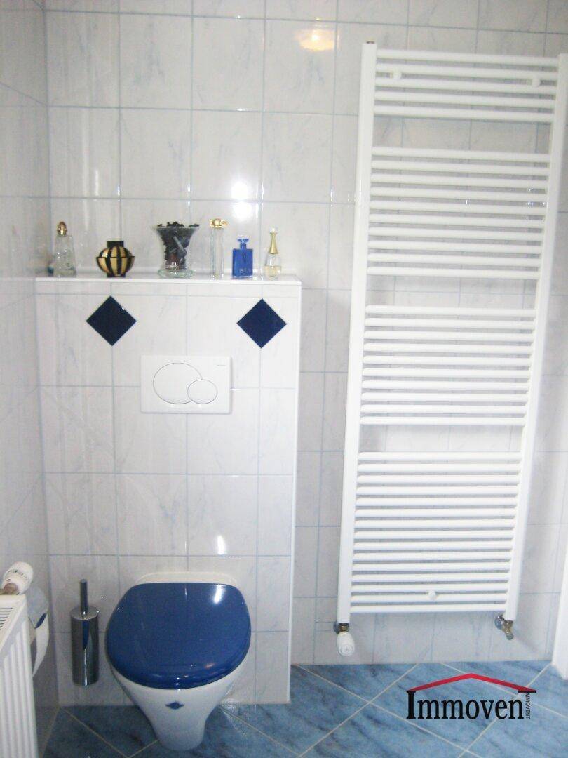 Modernes WC mit wandhängender Toilette, Handtuchheizkörper und blauen Bodenfliesen.