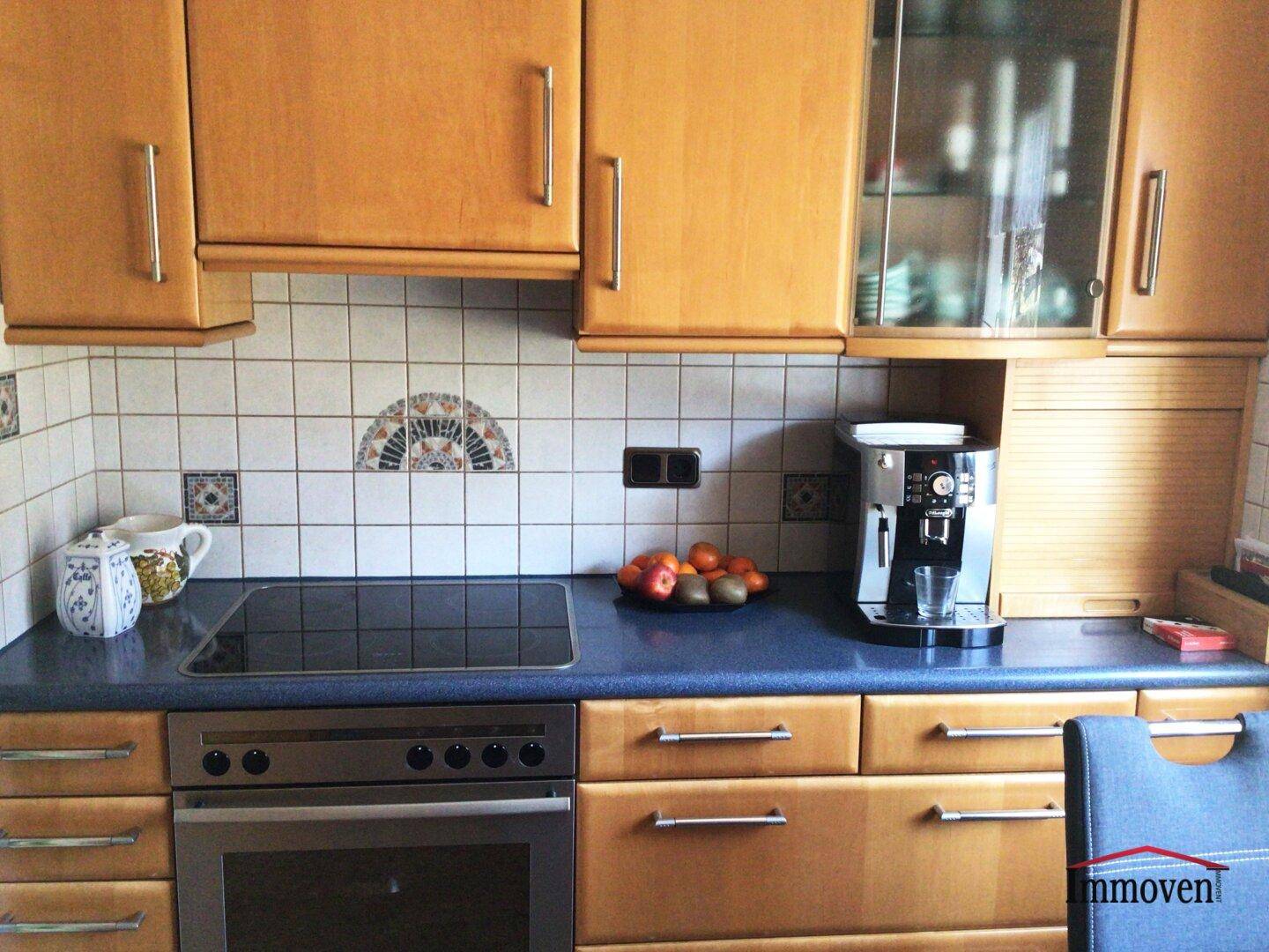 Funktionale Küche mit hellen Holzschränken, dunkler Arbeitsplatte und integriertem Kochfeld.