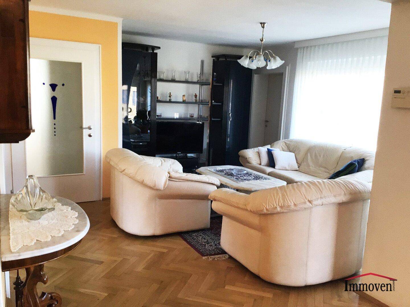Gemütliches Wohnzimmer mit beigen Ledersofas, Parkettboden und dunklen Schränken.