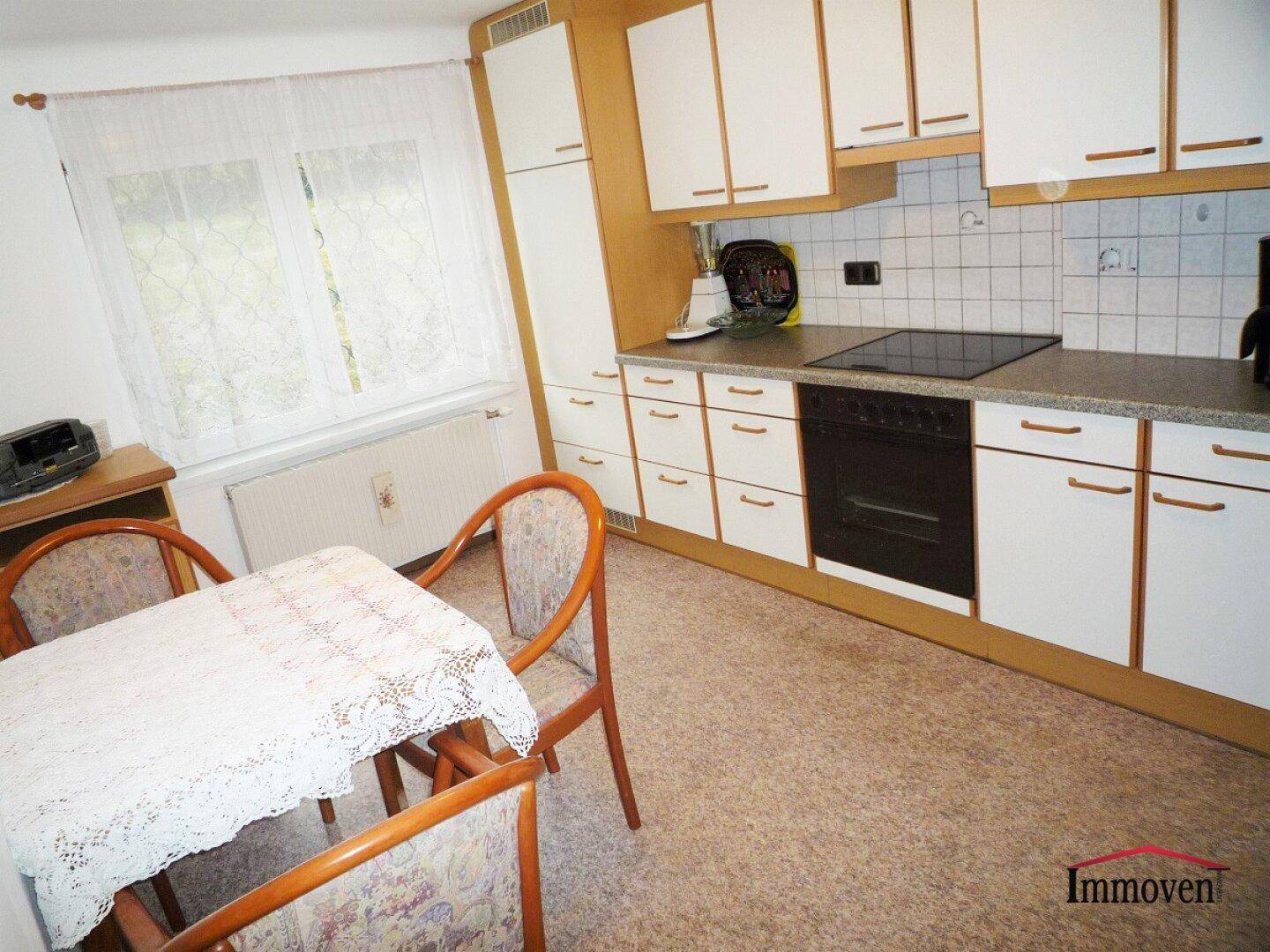 Helle Einbauküche mit weißen Schränken, Essbereich und Fenster, funktional eingerichtet.
