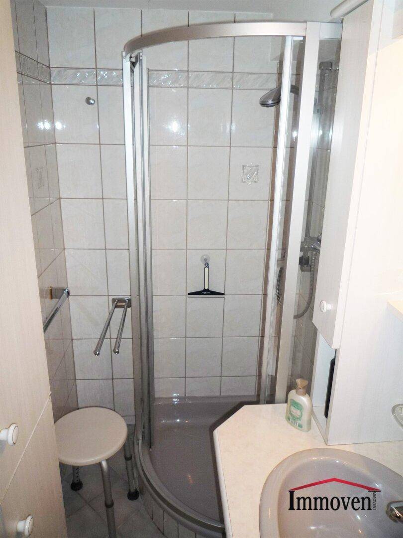 Kleines Badezimmer mit Duschkabine, Waschtisch und hellen Fliesen, funktional ausgestattet.