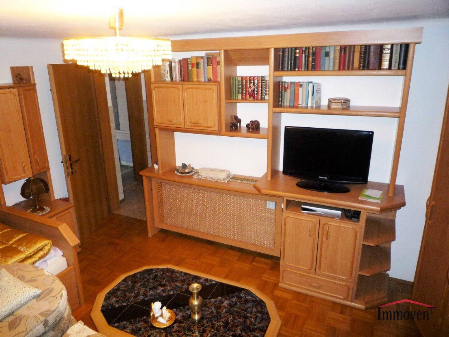 Wohnzimmer mit umfangreicher Holzschrankwand, Bücherregalen und Parkettboden.