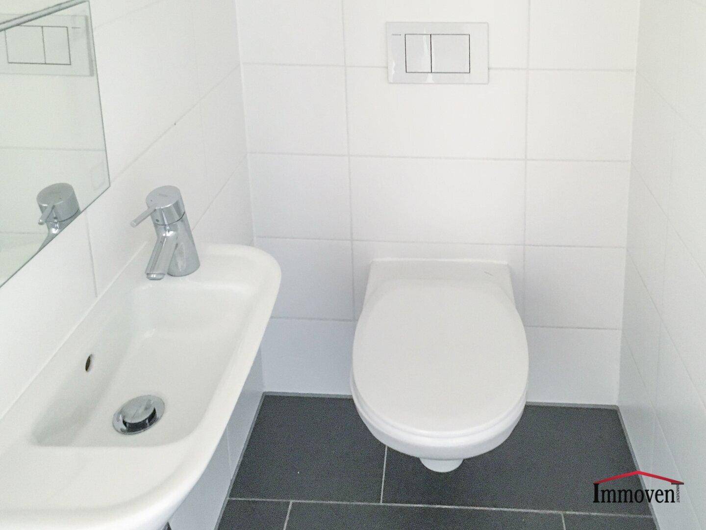 Separates Gäste-WC mit wandmontierter Toilette, kleinem Waschbecken und dunklem Fliesenboden.