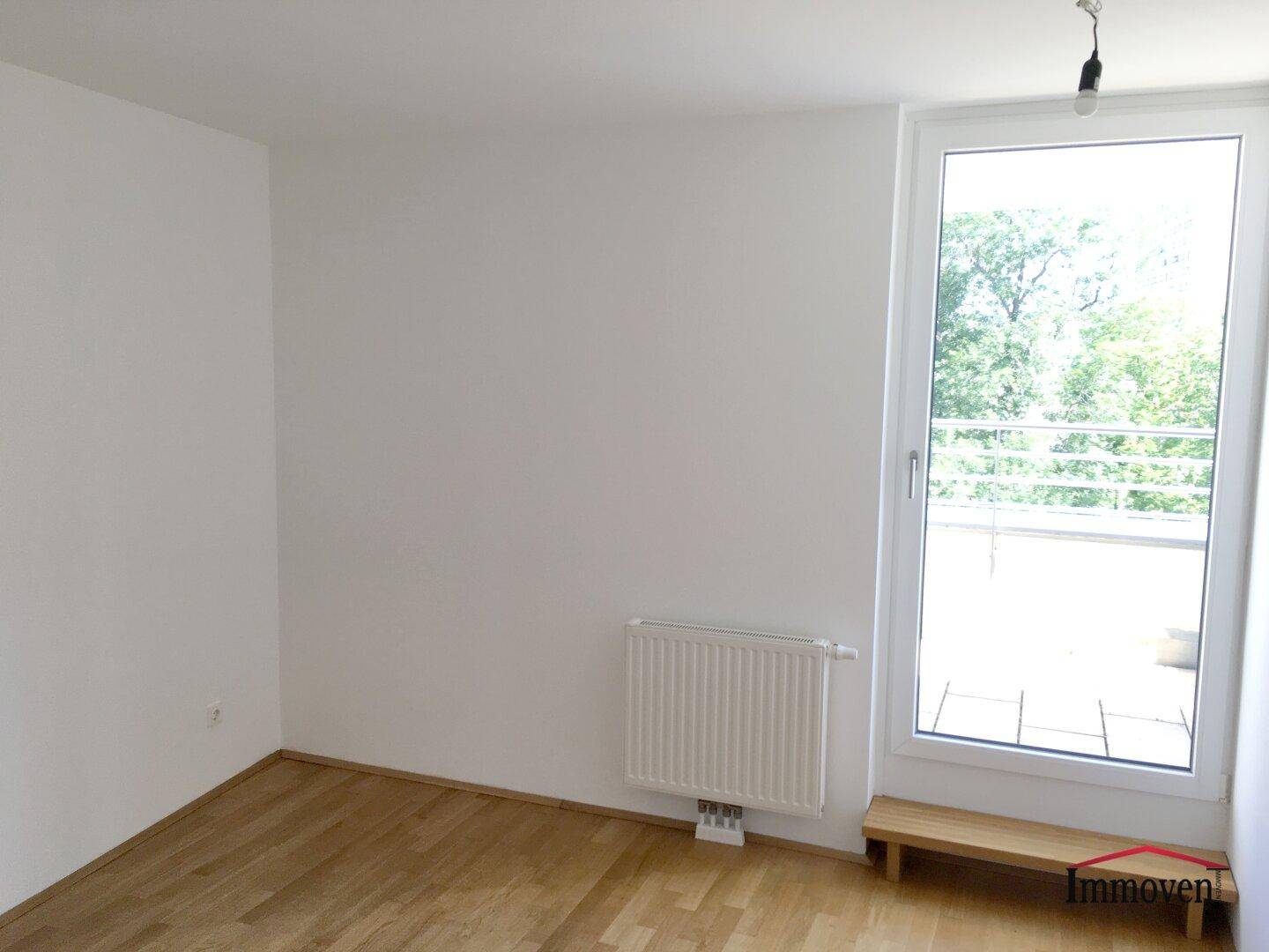 Lichtdurchflutetes Schlafzimmer mit Parkettboden und großem Fenster mit Blick ins Grüne.