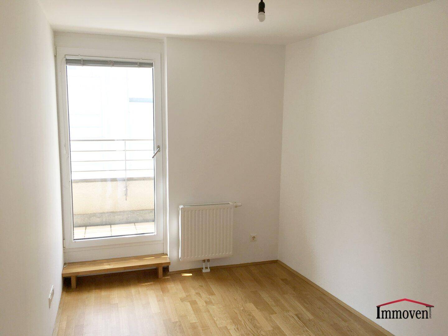 Helles Schlafzimmer mit Parkettboden, Heizkörper und Zugang zu einem Außenbereich.