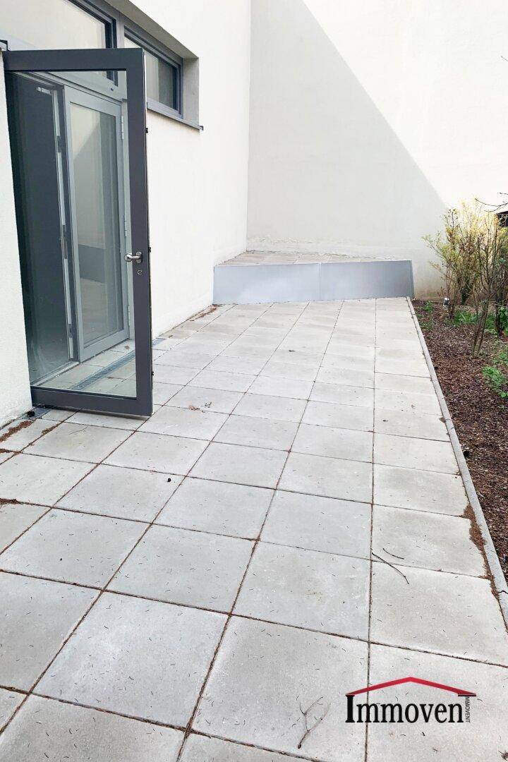 Gepflasterte Terrasse mit Zugang zum Gebäude und einem kleinen Beet am Rand.