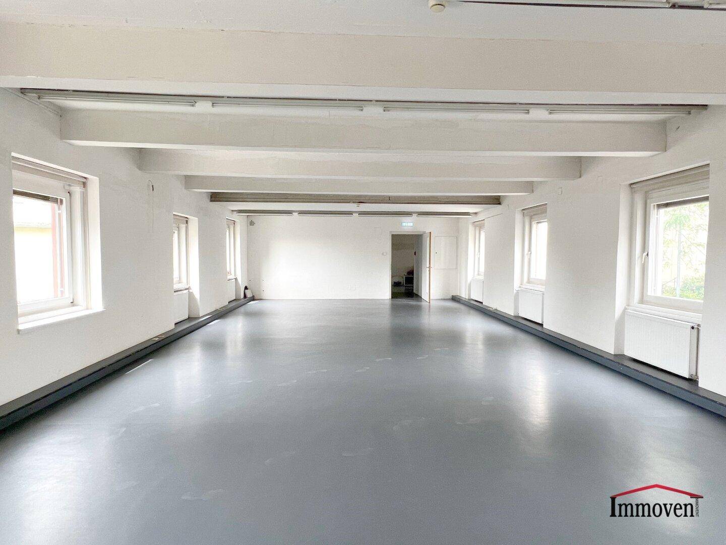 Heller, weitläufiger Büroraum mit vielen Fenstern und sichtbaren Deckenbalken, bereit zur individuellen Gestaltung.