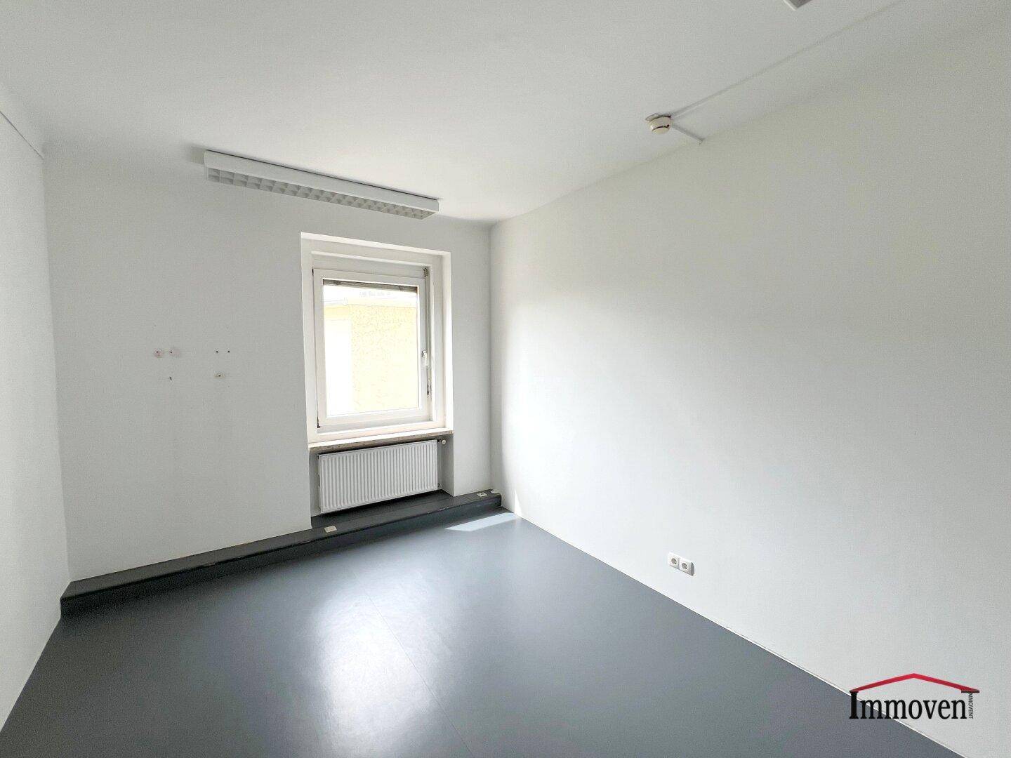 Kleinerer Büroraum mit einem Fenster, Heizkörper und grauem Bodenbelag, geeignet als Einzelbüro.