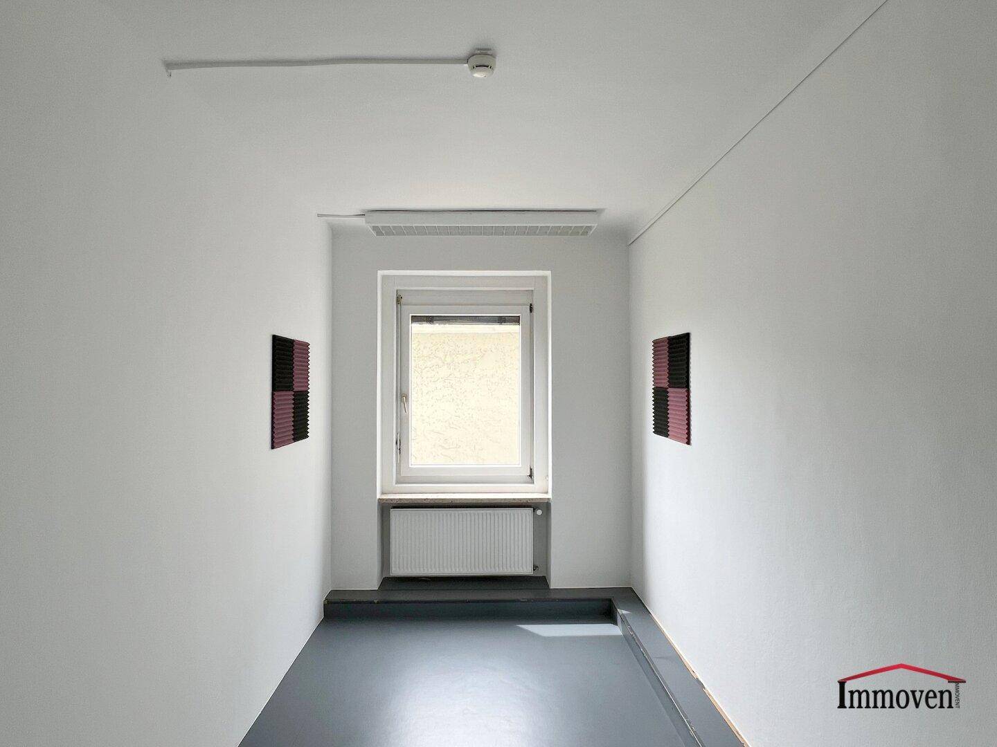 Schmaler Raum mit einem Fenster und zwei roten Akustikpaneelen an den Wänden, möglicherweise ein Flur.