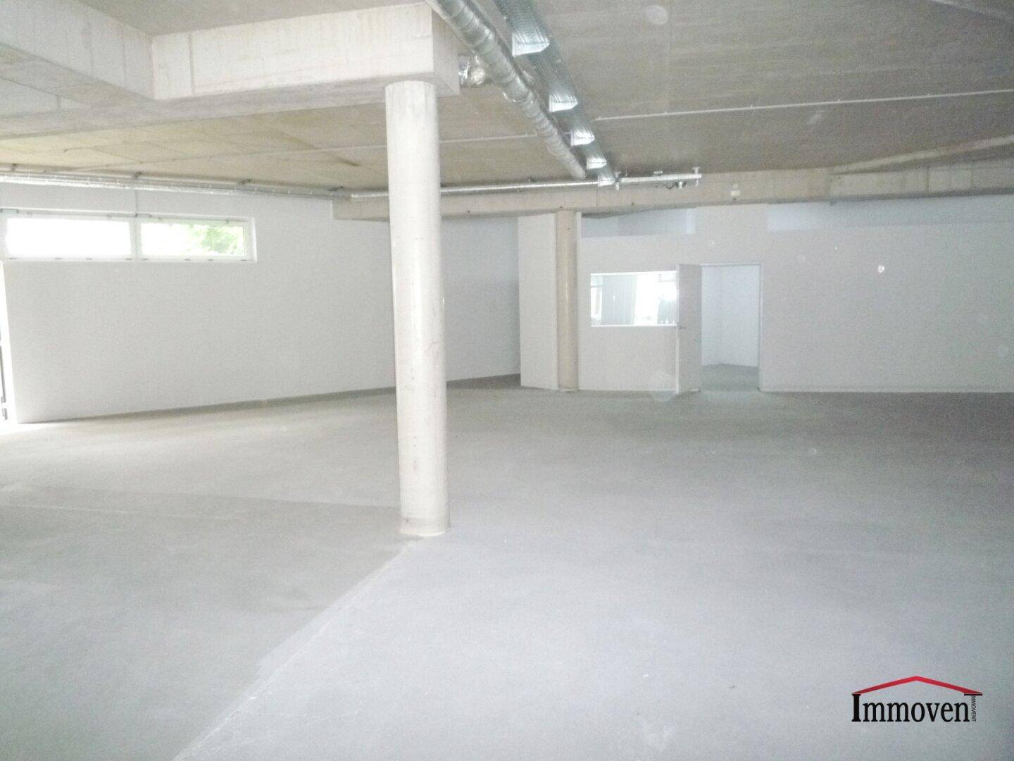 Großer, heller Gewerberaum im Rohbauzustand mit hohen Decken und sichtbaren Betonelementen und Installationen.