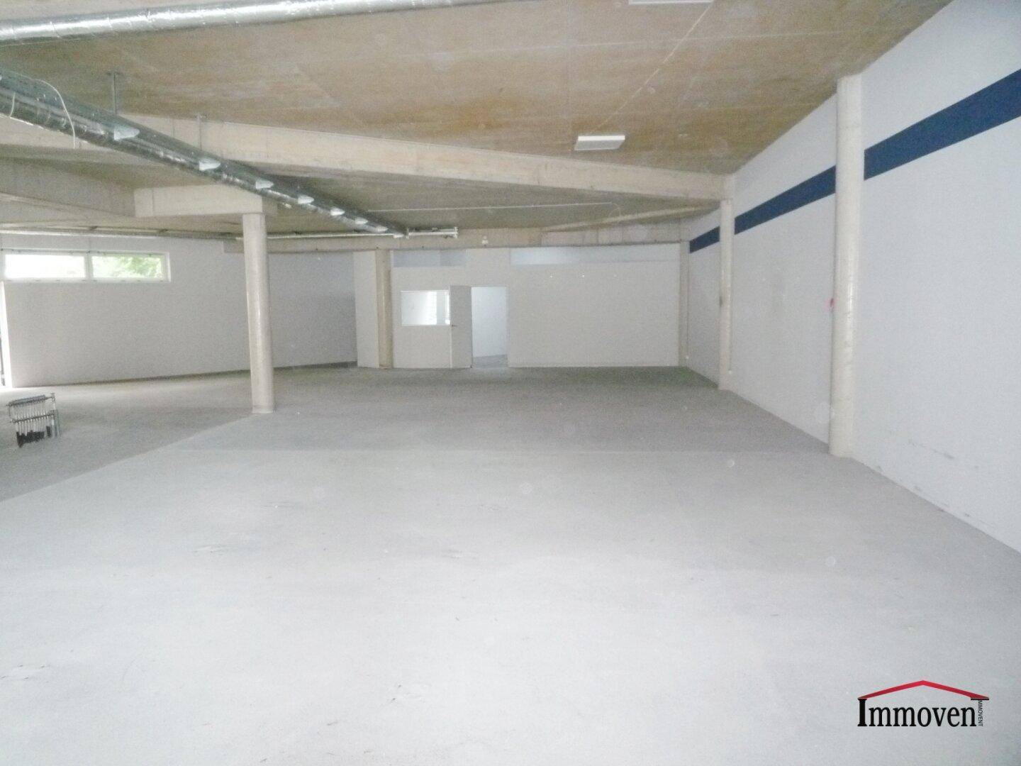 Weitläufiger Gewerberaum mit Betonboden, hohen Decken und blauen Akzentstreifen an den Wänden im Rohbau.