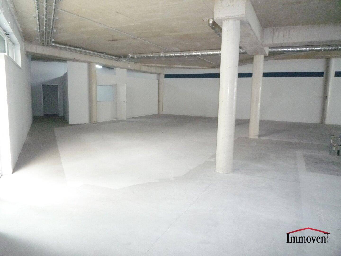 Geräumiger Gewerberaum mit Betonboden, Säulen und einem Blick auf den Eingangsbereich mit natürlichem Licht.