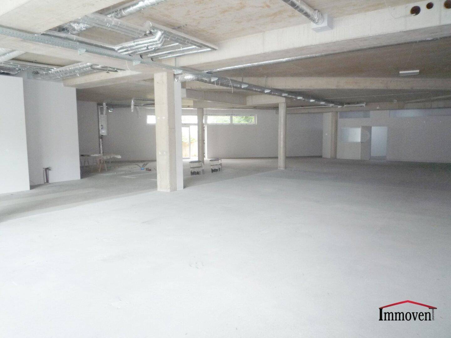Weitläufiger Gewerberaum im Rohbauzustand mit Betonsäulen und natürlichem Lichteinfall durch die Fenster.