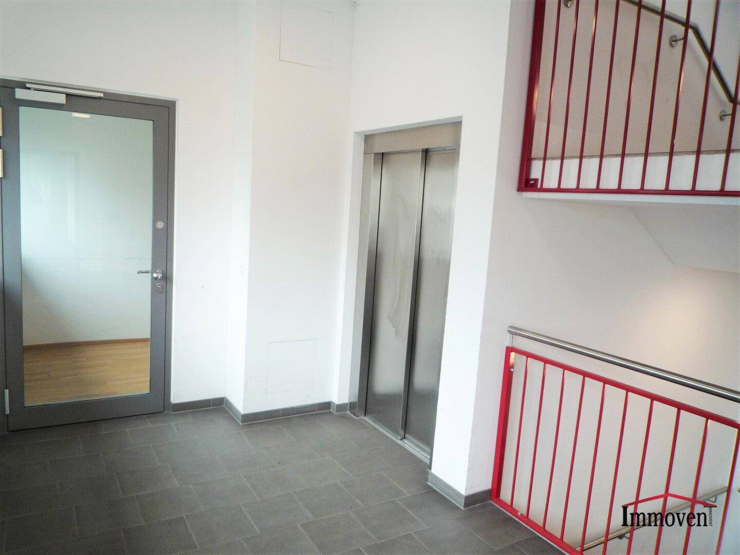 Eingangsbereich mit Aufzug, Treppe und Fliesenboden in einem Mehrfamilienhaus.