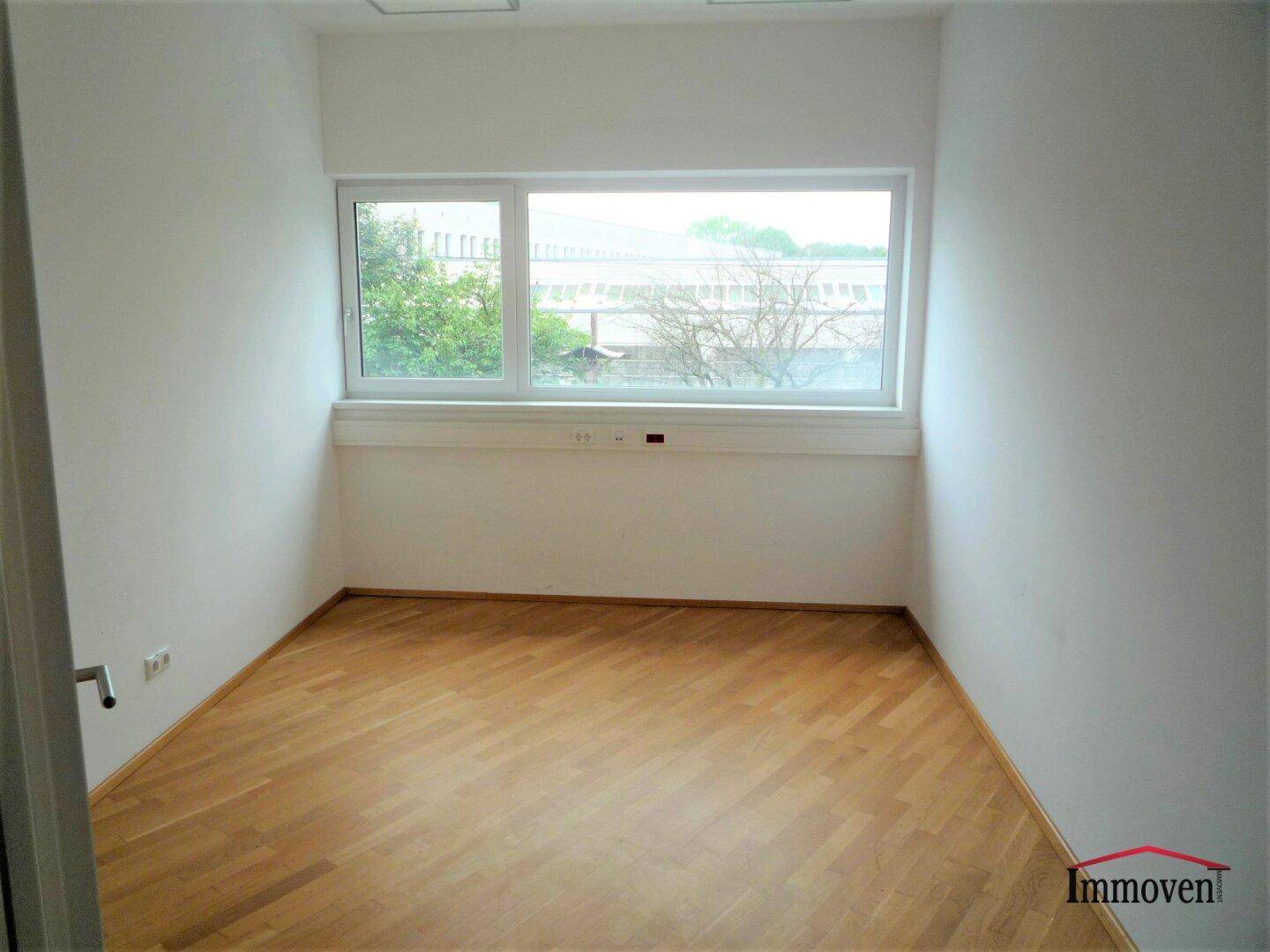 Kleiner Büroraum mit Holzboden und einem großen Fenster mit Blick ins Grüne.