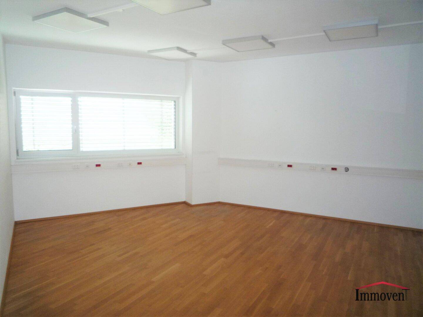 Geräumiger Büroraum mit Holzboden, großen Fenstern und Deckenbeleuchtung.