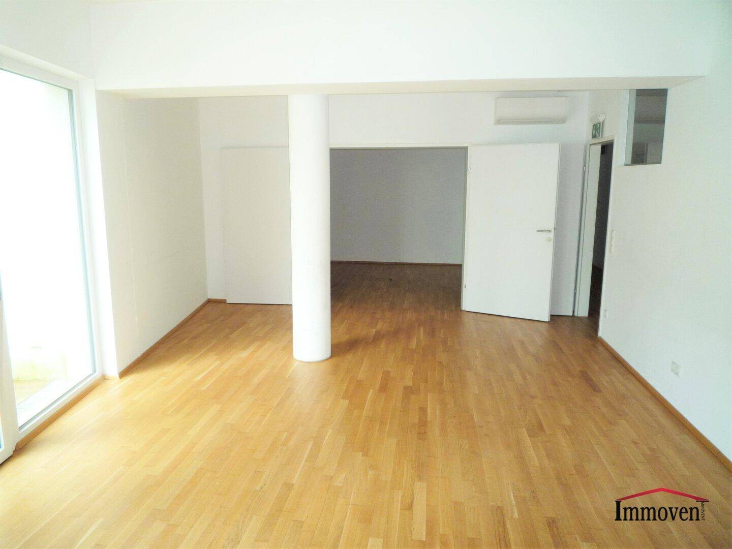 Heller Büroraum mit Holzboden, Säule und großen Fenstern mit viel Tageslicht.