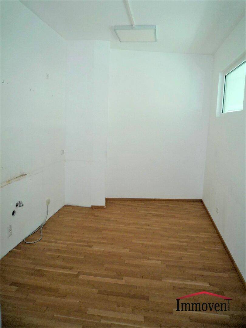Kleiner, leerer Raum mit Holzboden, weiß gestrichenen Wänden und einem Fenster.