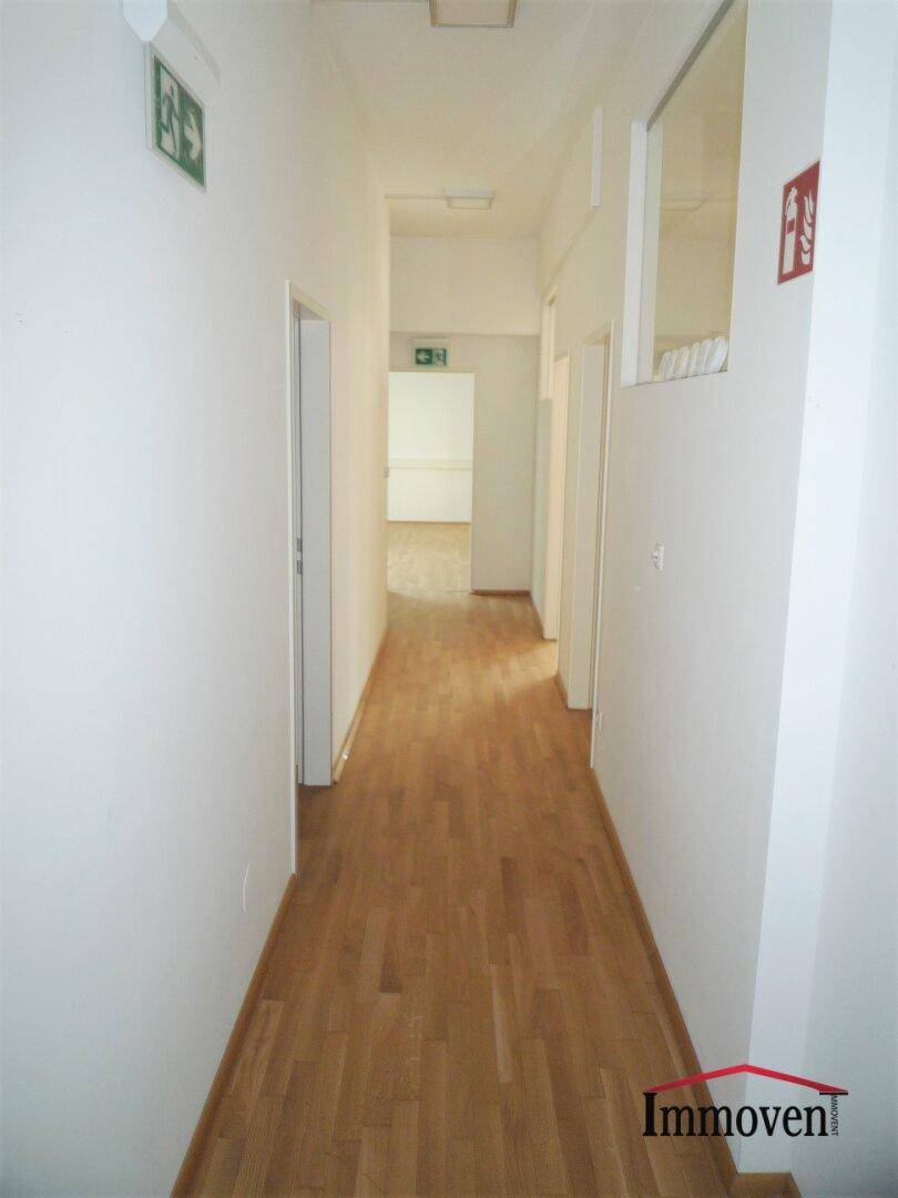 Langer Flur mit Holzboden, weißen Wänden und mehreren Türen zu Büroräumen.