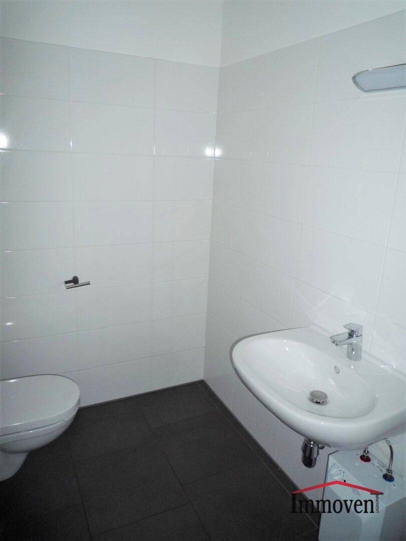 Modernes WC mit weißen Fliesen, dunklem Boden und einem Waschbecken.