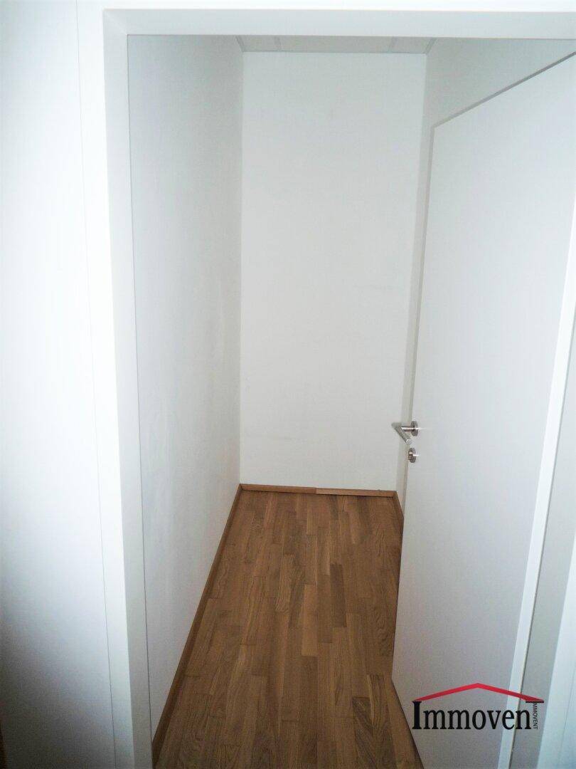 Schmaler Abstellraum oder Flur mit Holzboden und einer weißen Tür.