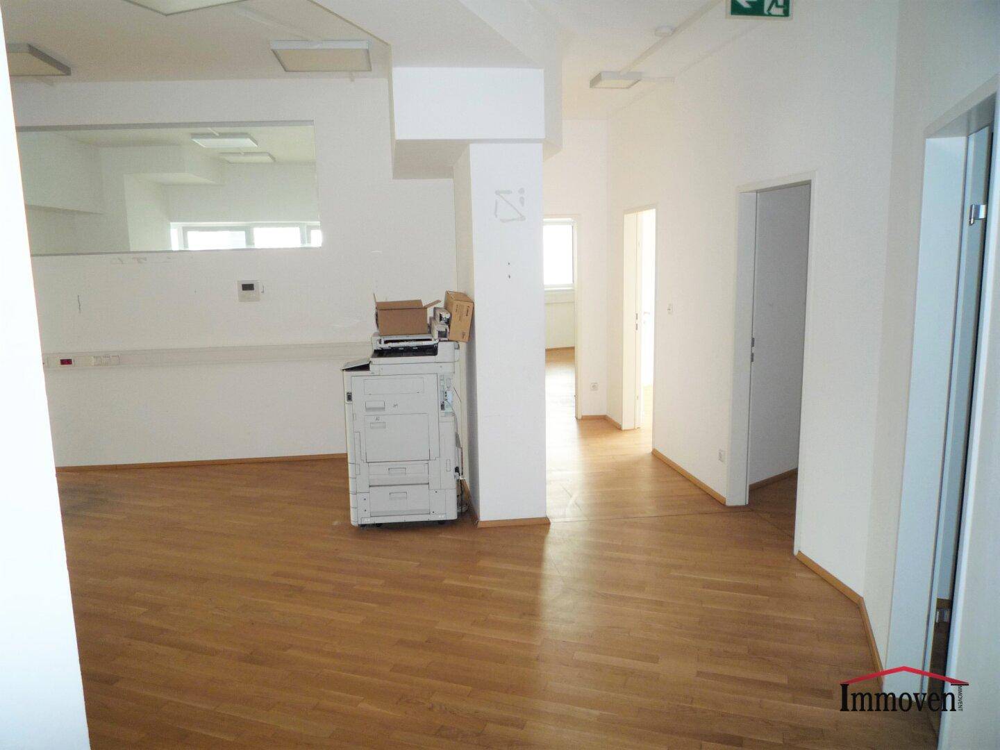 Offener Bürobereich mit Holzboden, Säule und einem Kopiergerät im Vordergrund.