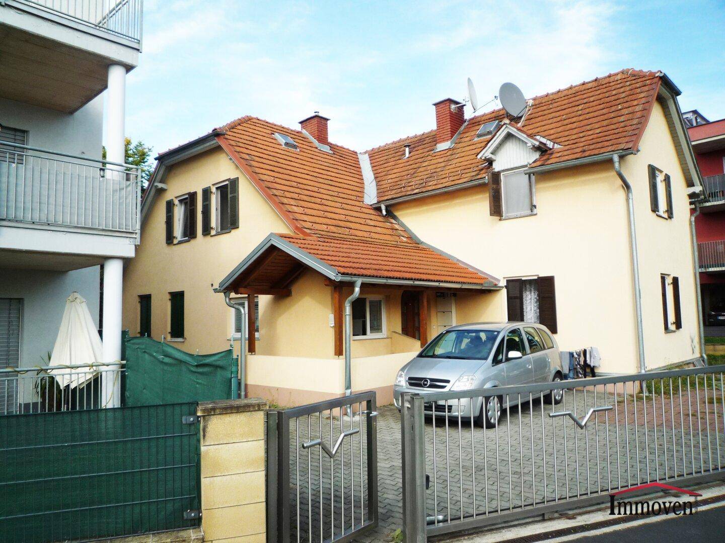 Gesamtansicht des Hauses mit gepflasterter Einfahrt und dem benachbarten modernen Wohngebäude.