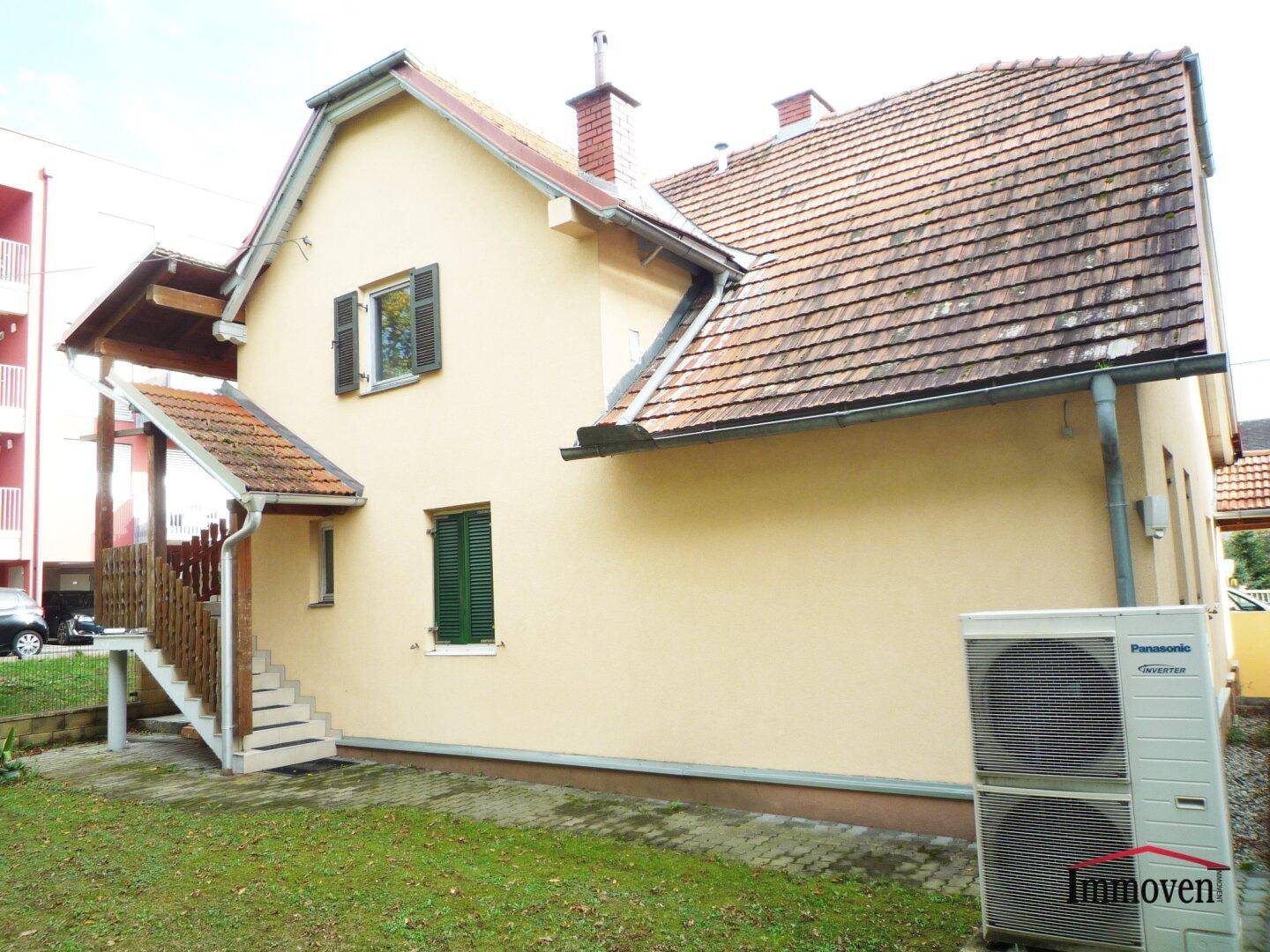Rückseite des Hauses mit Außentreppe, kleiner Rasenfläche und einer Wärmepumpe.