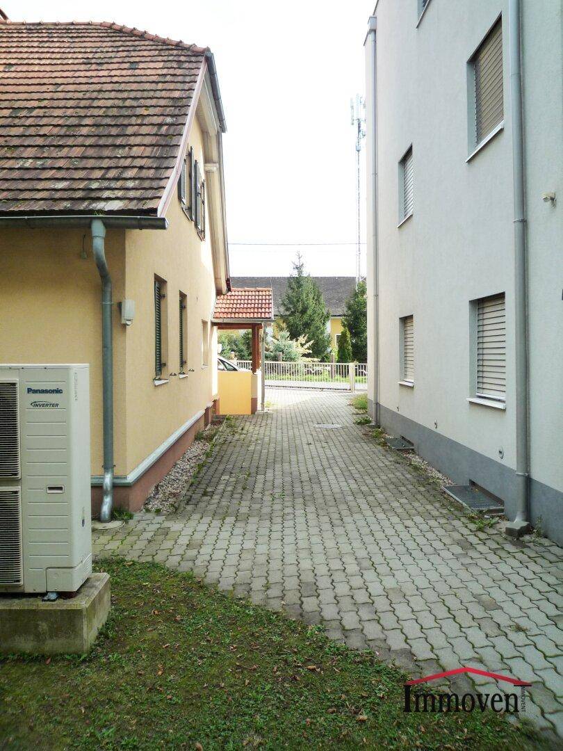 Schmaler gepflasterter Weg zwischen zwei Gebäuden, der zu einem hinteren Bereich führt.
