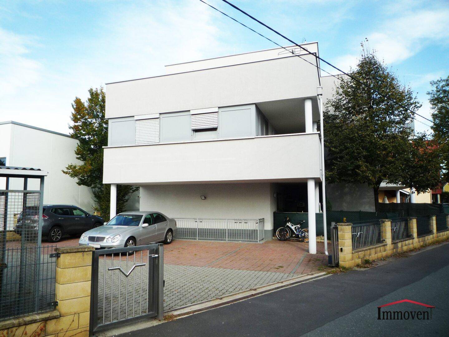 Moderne Fassade des Apartmentgebäudes mit überdachten Parkplätzen und Balkonen.
