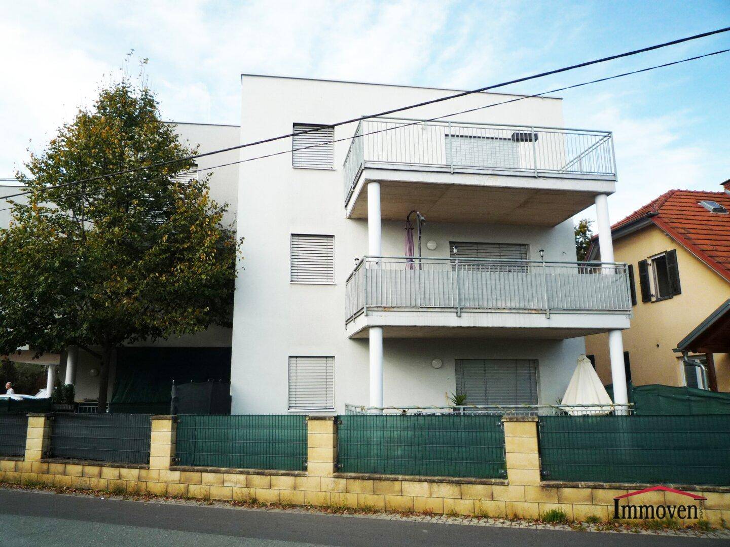 Ansicht des modernen Apartmentgebäudes mit mehreren Balkonen und einer grünen Umzäunung.