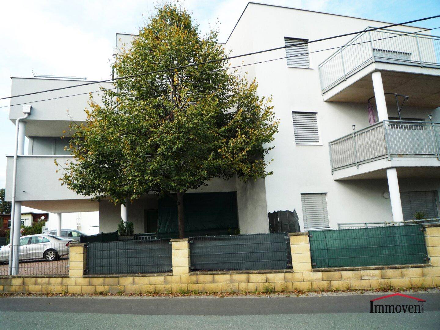 Vorderansicht des modernen Apartmentgebäudes mit einem Baum und überdachten Parkplätzen.