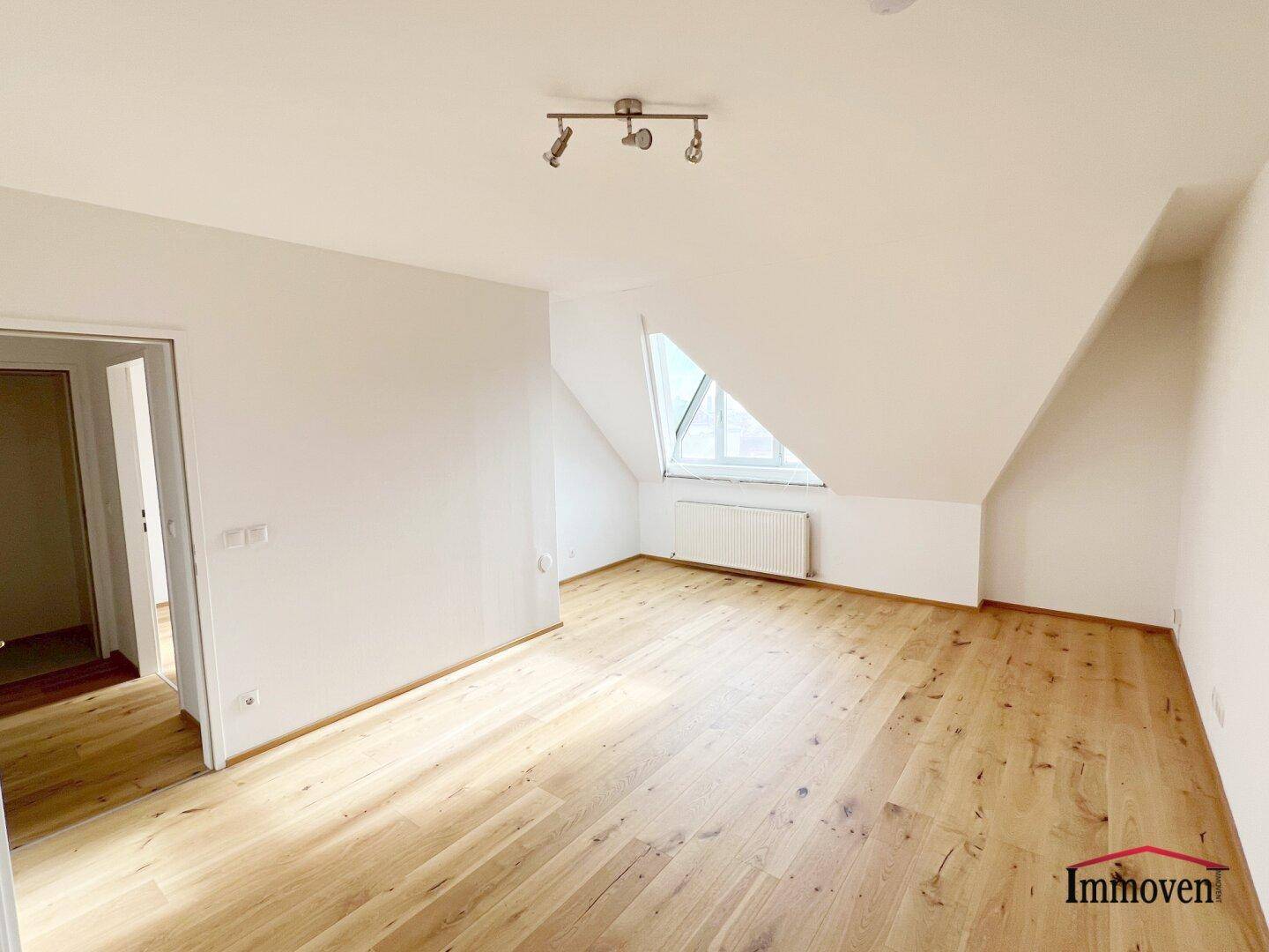 Heller Raum mit Holzboden und Dachschräge, bietet Zugang zu einem weiteren Zimmer.