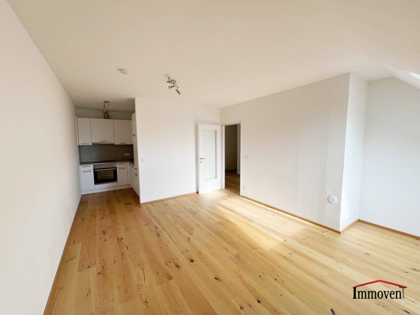 Wohnbereich mit Holzboden und integrierter, kompakter Küchenzeile in modernem Design.